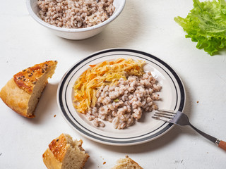 Vegan breakfast of barley and stewed cabbage on a white plate, near chunks of homemade bread.