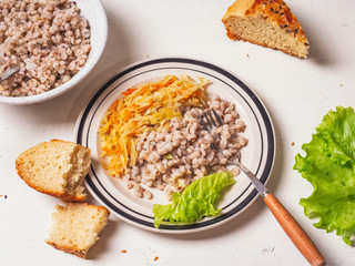 Vegan breakfast of barley and stewed cabbage on a white background, next to chunks of homemade bread and leaves of green leaf lettuce.