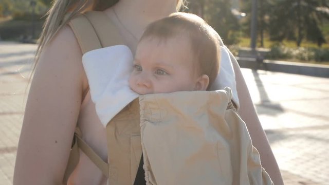 Young happy mom with baby girl in ergo backpack walking in the Park