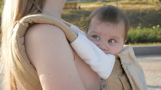 Young happy mom with baby girl in ergo backpack walking in the Park
