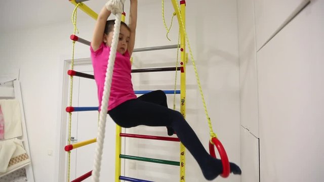 Girl smiling and hanging by hand on wall horizontal bar.