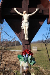 A roadside calvary with a figurine of Jesus on a cross with flowers in autumn time