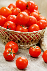 Small red tomatoes in a wicker basket on an old wooden table. Ripe and juicy cherry