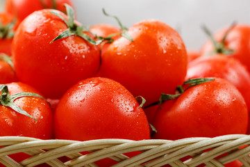Small red tomatoes in a wicker basket on an old wooden table. Ripe and juicy cherry