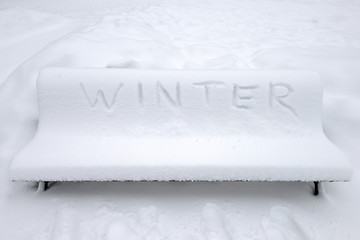 Park bench covered with snow and written Winter in English