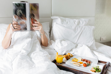 Fototapeta na wymiar Woman having breakfast in bed and reading magazine
