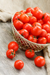 Small red tomatoes in a wicker basket on an old wooden table. Ripe and juicy cherry