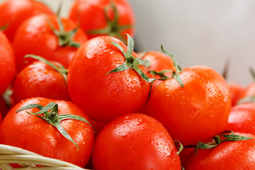 Small red tomatoes in a wicker basket on an old wooden table. Ripe and juicy cherry