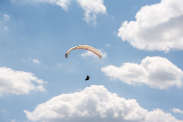 Lone paraglider seen from below gliding through the air over partially clouded skies.