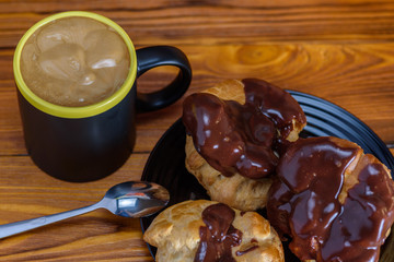 Coffee and chocolate eclairs on a wooden background