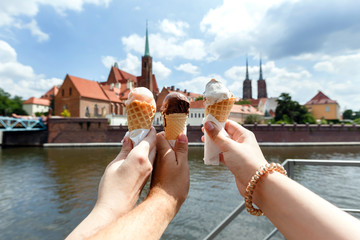 Three human hands hold ice cream on a background of a old churches of the historic center of Wroclaw.