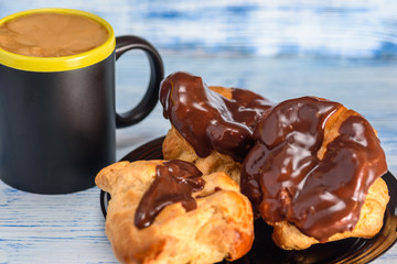 Coffee and chocolate eclairs on a wooden background