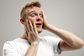 Wow. Attractive male half-length front portrait on gray studio backgroud. Young emotional surprised...