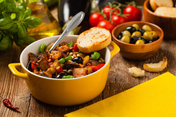 Traditional Italian caponata, served with croutons in a yellow, sunny pot. Decorated with basil and...