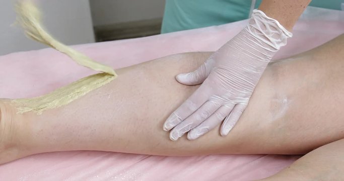 Woman having sugaring depilation on legs in beauty salon. Hands of a beautician making hair removal process with sugar paste, closeup
