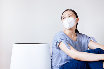 Fototapeta na wymiar Masked Asian women sitting beside the air purifier close up. Pollution and unhealthy life concept.