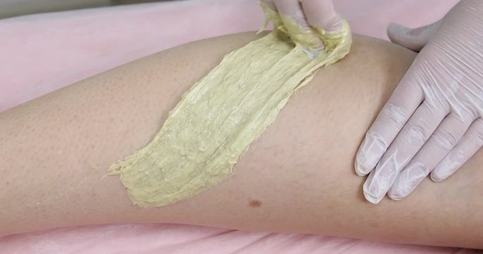 Woman having sugaring depilation on legs in beauty salon. Hands of a beautician making hair removal process with sugar paste, closeup