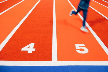 Blur motion part of boy is running on colorful atheltic running track with white numbers in...