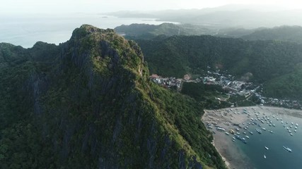 Aerial drone shot of high mountain covered with tropical forest and boats anchored in the bay. Tropical landscape. Travel concept Philippines,El Nido.