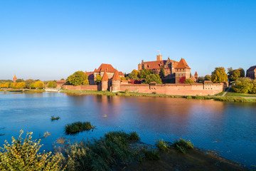 Fototapeta na wymiar Medieval Malbork (Marienburg) Castle in Poland, main fortress of the Teutonic Knights at the Nogat river. Aerial view in fall in sunset light.