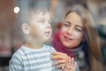 view through the panoramic window  to a happy couple of mom and child boy. family looks through the cafe windows, the mother shows a finger in the window and the son watches. selective focus