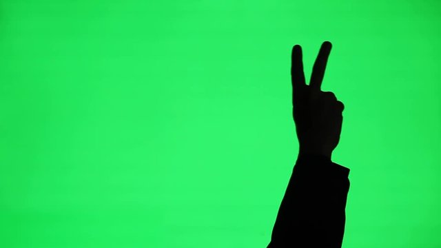 The silhouette of a man's hand doing a peace or victory gesture on a green screen background.