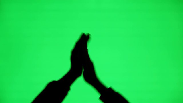 The silhouette of a man's hands clapping on a green screen background.