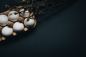 White easter eggs in carton box and willow branches isolated on black background. Easter holiday...