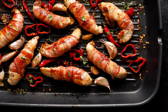 Spicy chicken meat, Grilled chicken tenderloin wrapped with bacon with addition chili peppers, garlic and herbs on grill plate, close-up, top view