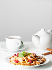 Belgian curd waffles with raspberries, banana, chocolate syrup.  Breakfast with tea on white background, side view, vertical