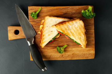 Broccoli cheese sandwiches on wooden cutting board, on concrete, slate background