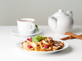 Belgian curd waffles with raspberries, banana, chocolate syrup.  Breakfast with tea on white background, side view