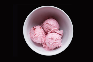 Three scoops of pink strawberry ice cream in white bowl on black background