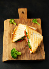Broccoli cheese sandwiches on wooden cutting board, on concrete, slate background