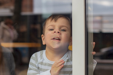 little boy has fun and shows a different grimace, presses his face to the glass in a panoramic...