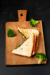 Broccoli cheese sandwiches on wooden cutting board, on wooden table
