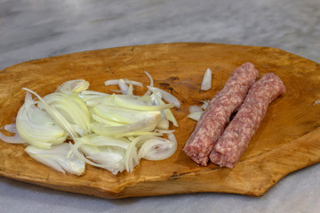 Chopped onion and two raw Kebapche (Balkan specialty of minced meat with spices) on a wooden board ready for the grill.