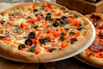 Pizza with fresh tomatoes, olives, mozzarella, olive oil and basil. On the background of Pizza with Pepperoni salami and chilli peppers.