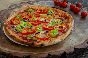 Pizza with tomato sauce, ham, egg, fresh green and red peppers, yellow cheese, olive oil and basil. On a wooden board against the background of cherry tomatoes.