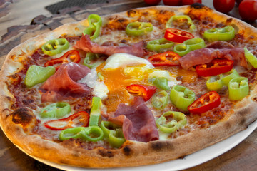 Pizza with tomato sauce, ham, egg, fresh green and red peppers, yellow cheese, olive oil and oregano.