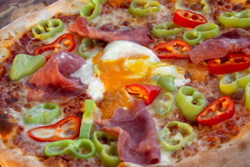 Pizza with tomato sauce, ham, egg, fresh green and red peppers, yellow cheese, olive oil and oregano. Closeup.
