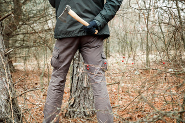 Naklejka premium man with an axe hiding in the autumn forest and going to make criminal