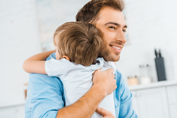 smiling handsome father hugging preschooler son at home