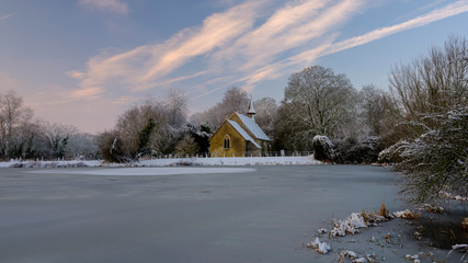 Frozen winter scene over Hartley Mauditt pond to St Leonard's Church, South Downs National Park,...