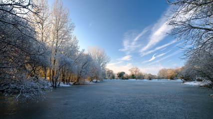 Frozen winter scene over Hartley Mauditt pond to St Leonard's Church, South Downs National Park, Hampshire, UK
