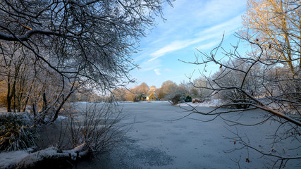 Frozen winter scene over Hartley Mauditt pond to St Leonard's Church, South Downs National Park, Hampshire, UK