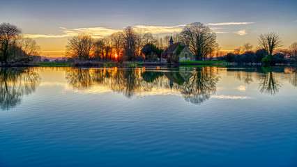 Sunset on Hartley Mauditt pond towards St Leonard's Church, South Downs National Park, Hampshire, UK