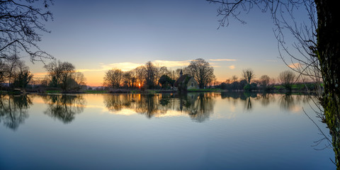 Sunset on Hartley Mauditt pond towards St Leonard's Church, South Downs National Park, Hampshire, UK