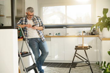 Mature handyman leaning on ladder in modern kitchen