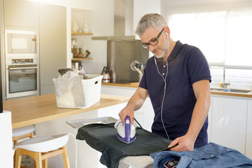 Smiling mature man ironing clean laundry at home